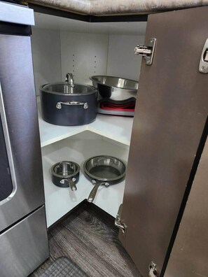 A compact kitchen with stainless steel appliances, including a stove, a large pot, and two frying pans. - Elegant Family Home by Stadium, Airport, Shopping (Regina)