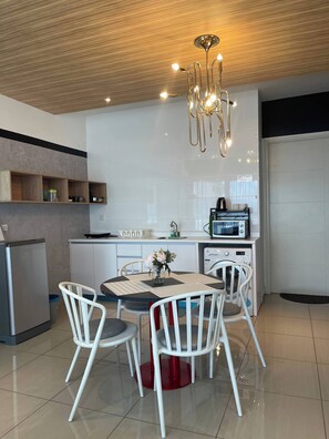 A modern kitchen with white cabinets, a dining table with chairs, a refrigerator, a microwave, and a hanging light fixture. - Arte Ampang Klcc 2 BR Homestay, 4-6 pax (Kuala Lumpur)