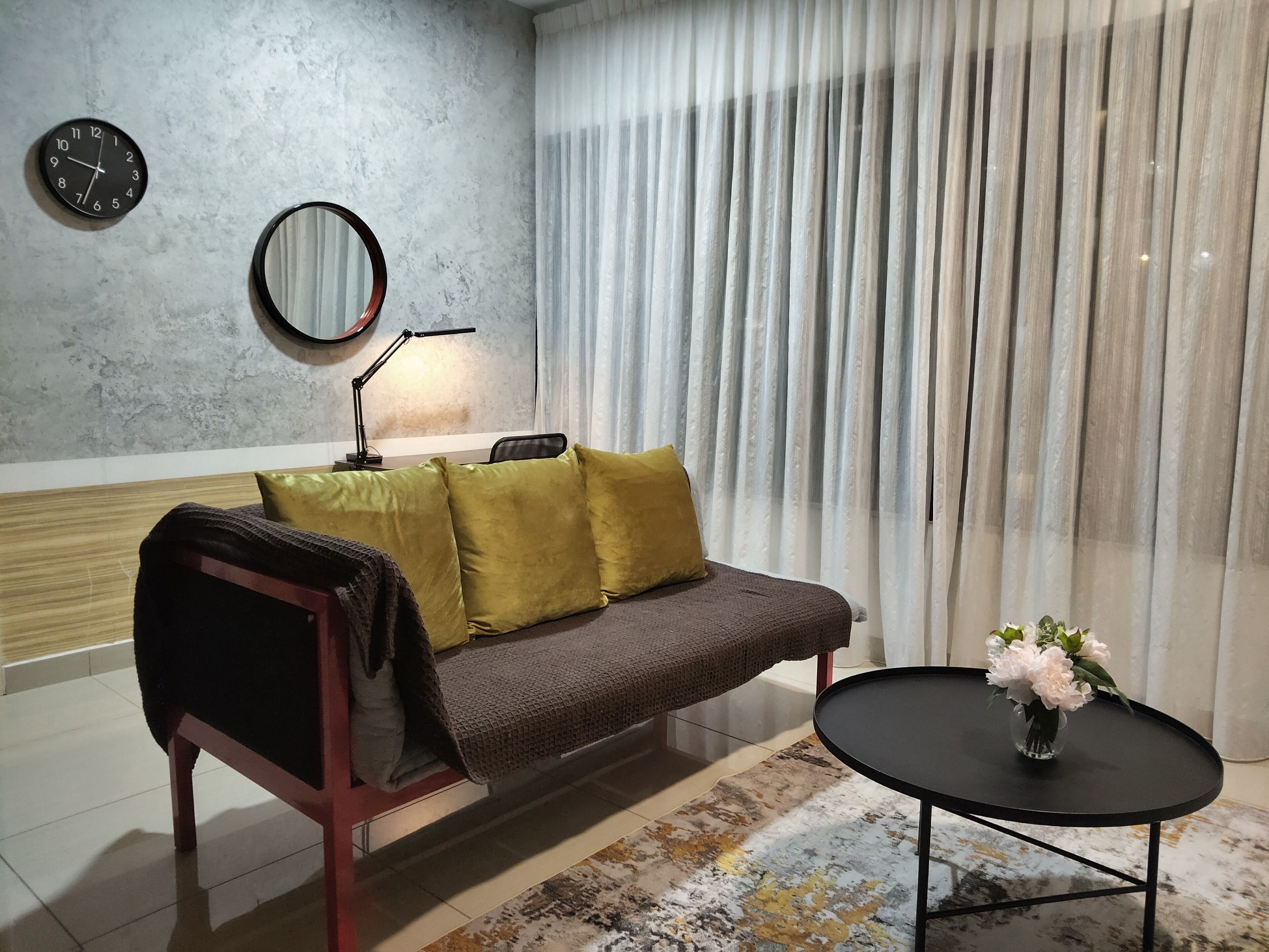 Ein modernes Wohnzimmer mit einer Couch, einem runden Spiegel, einer Lampe und einem kleinen Tisch mit Blumen.