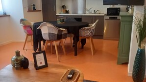 A modern living room with a dining area, kitchen, and a flat-screen TV mounted on the wall.