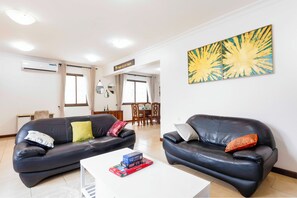 Sala de estar com dois sofás de couro preto, uma mesa de centro branca e um espaço de jantar ao fundo.