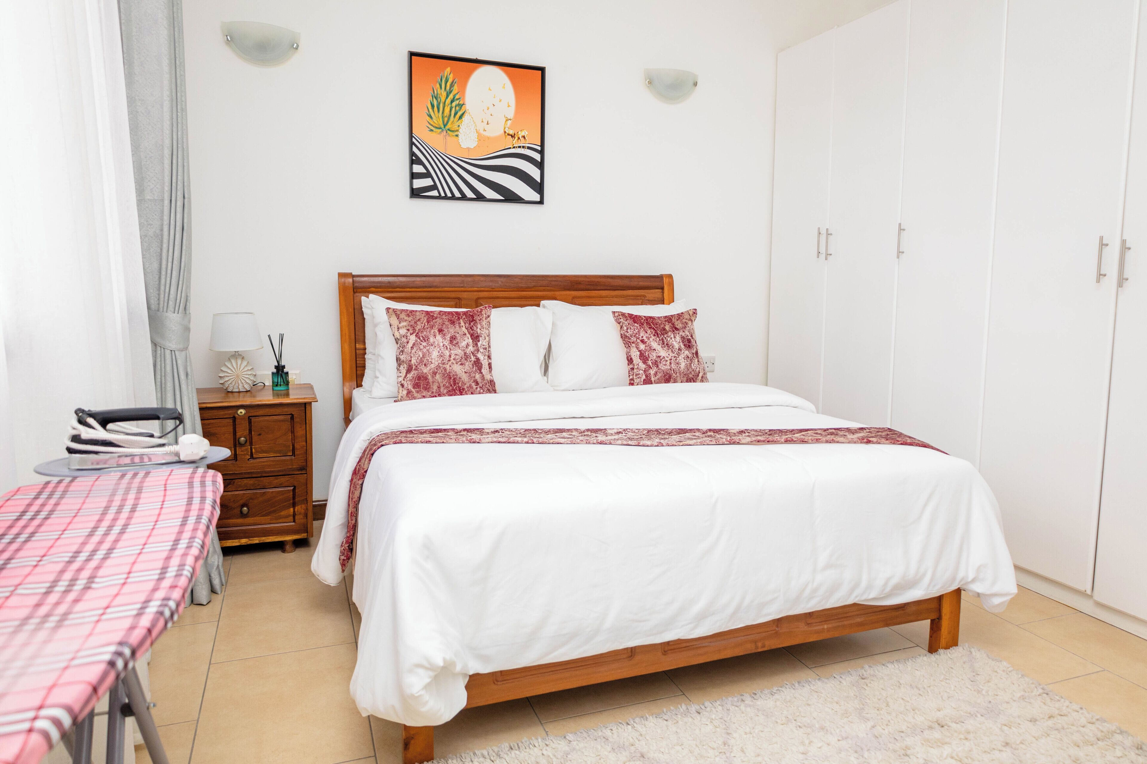 A bedroom with a wooden bed, white bedding, a small bedside table with a lamp, a chair, and a wardrobe.