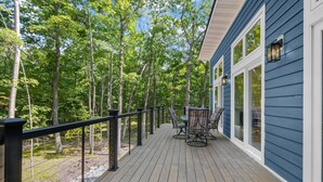 Una terraza de madera con mobiliario exterior, rodeada de árboles.