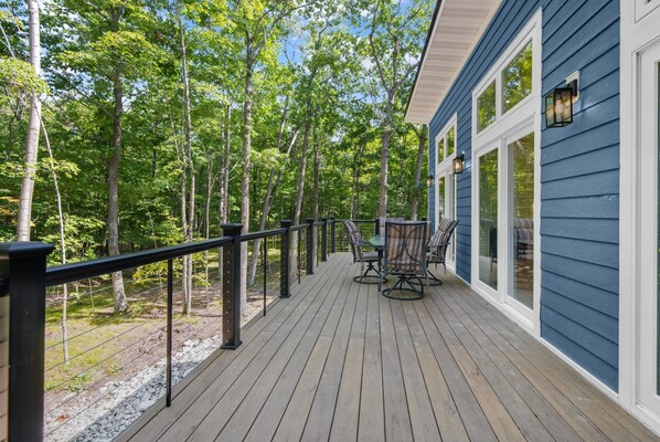 Una terraza de madera con mobiliario exterior, rodeada de árboles.