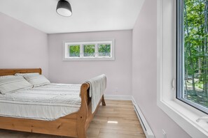 Ein Schlafzimmer mit einem hölzernen Bett, einem Fenster mit Blick auf Bäume und einer Deckenleuchte.