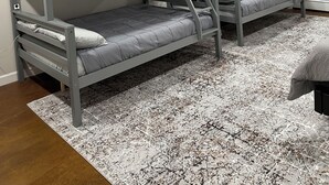 Habitación con literas, techo blanco, una puerta blanca y un tapete estampado en el suelo.