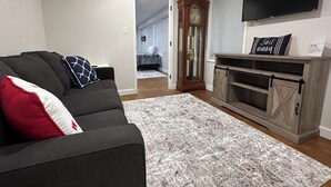 Una sala de estar con un sofá de color oscuro, un tapete estampado, un mueble de entretenimiento de madera y un televisor de pantalla plana.
