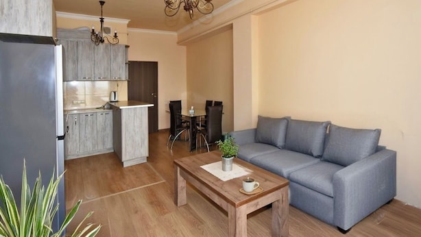 A modern living room with a grey sofa, wooden coffee table, and a dining area with a table and chairs.