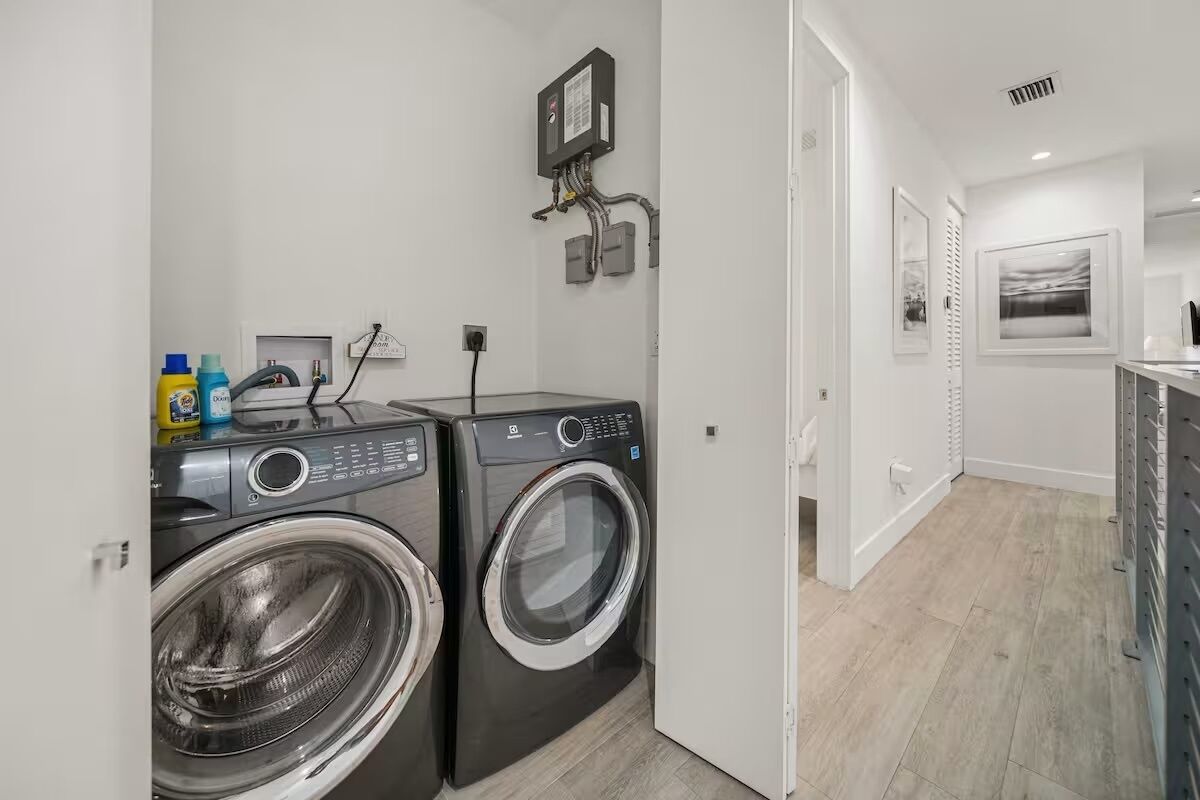 A laundry area with two front-loading washing machines, a control panel, and a wall-mounted electrical box.