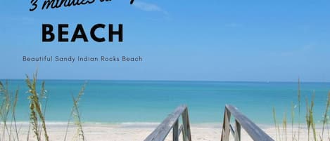 A wooden boardwalk leading to a beach with clear turquoise water and a clear sky.