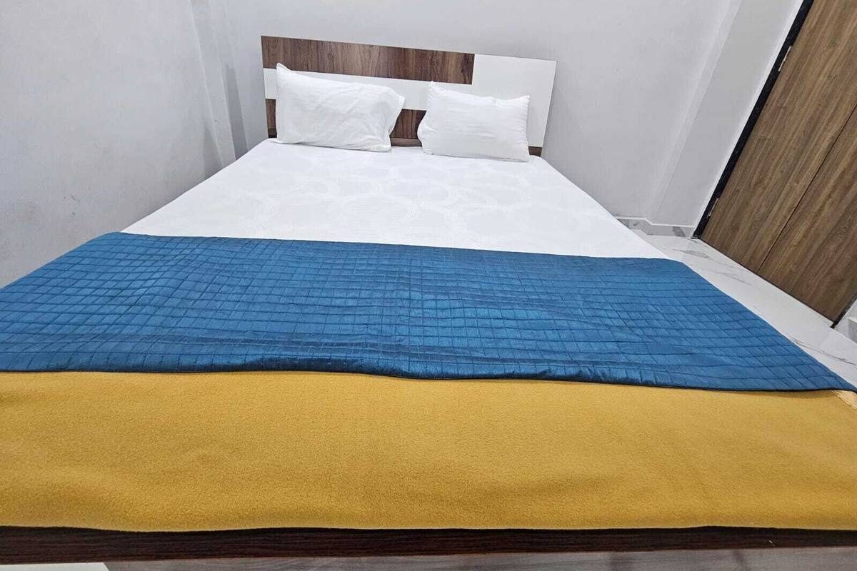 Un lit avec un matelas blanc et deux oreillers blancs, une couverture matelassée bleue et une couverture jaune.