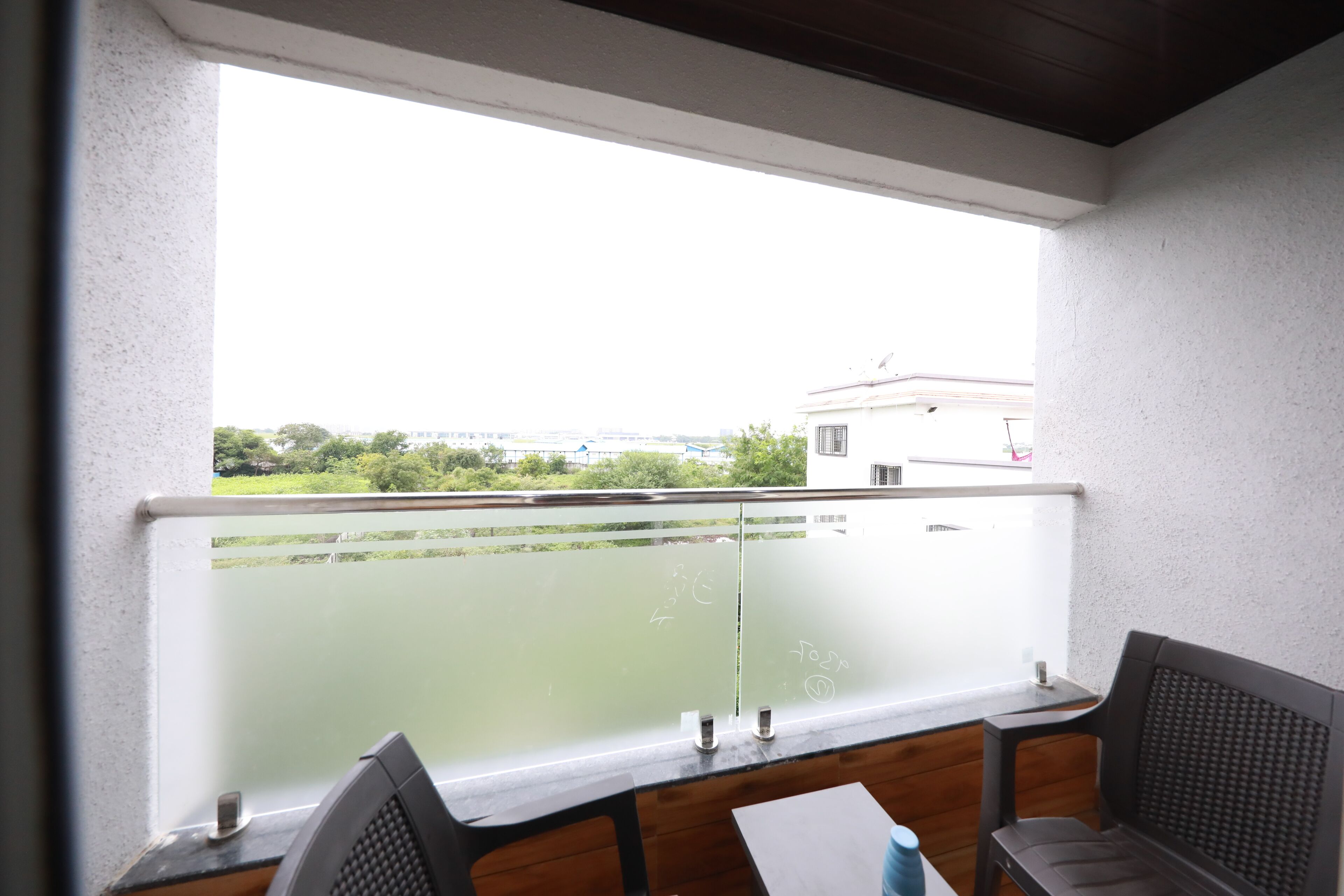 A balcony with a view of greenery and buildings, a table with chairs, and a window with frosted glass.