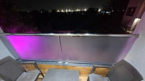 Un balcon avec deux chaises et une table, donnant sur une vue panoramique de la ville la nuit.