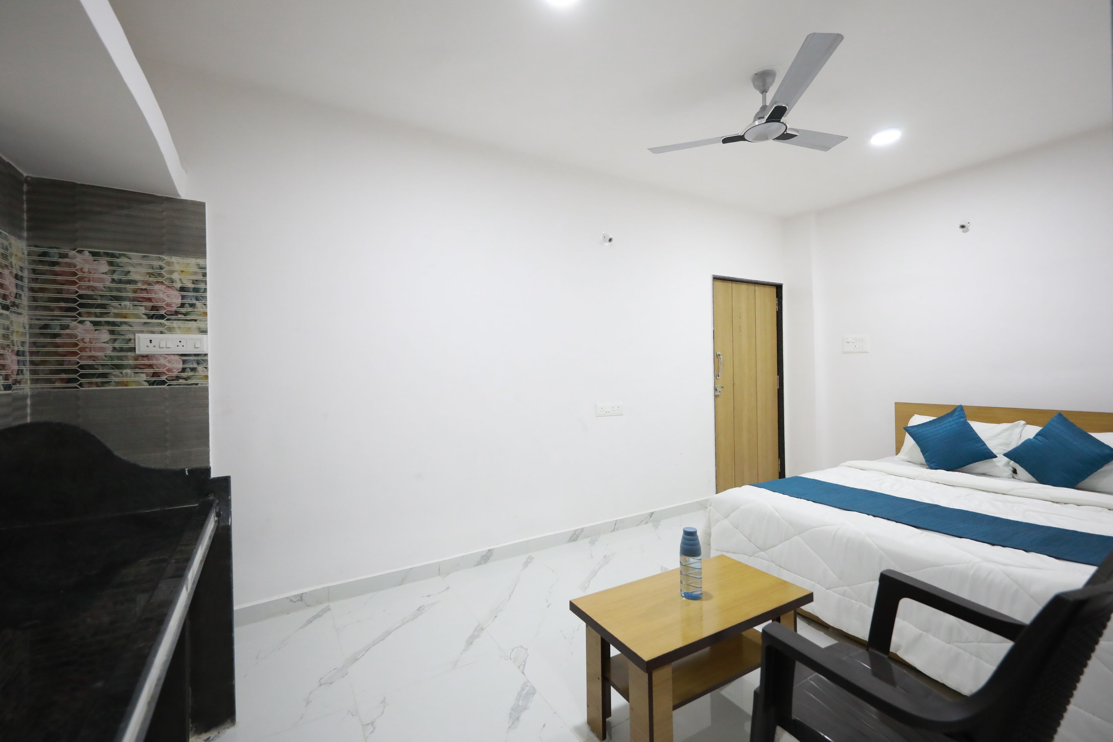 Habitación de hotel con cama, escritorio, silla, ventilador de techo y una puerta.
