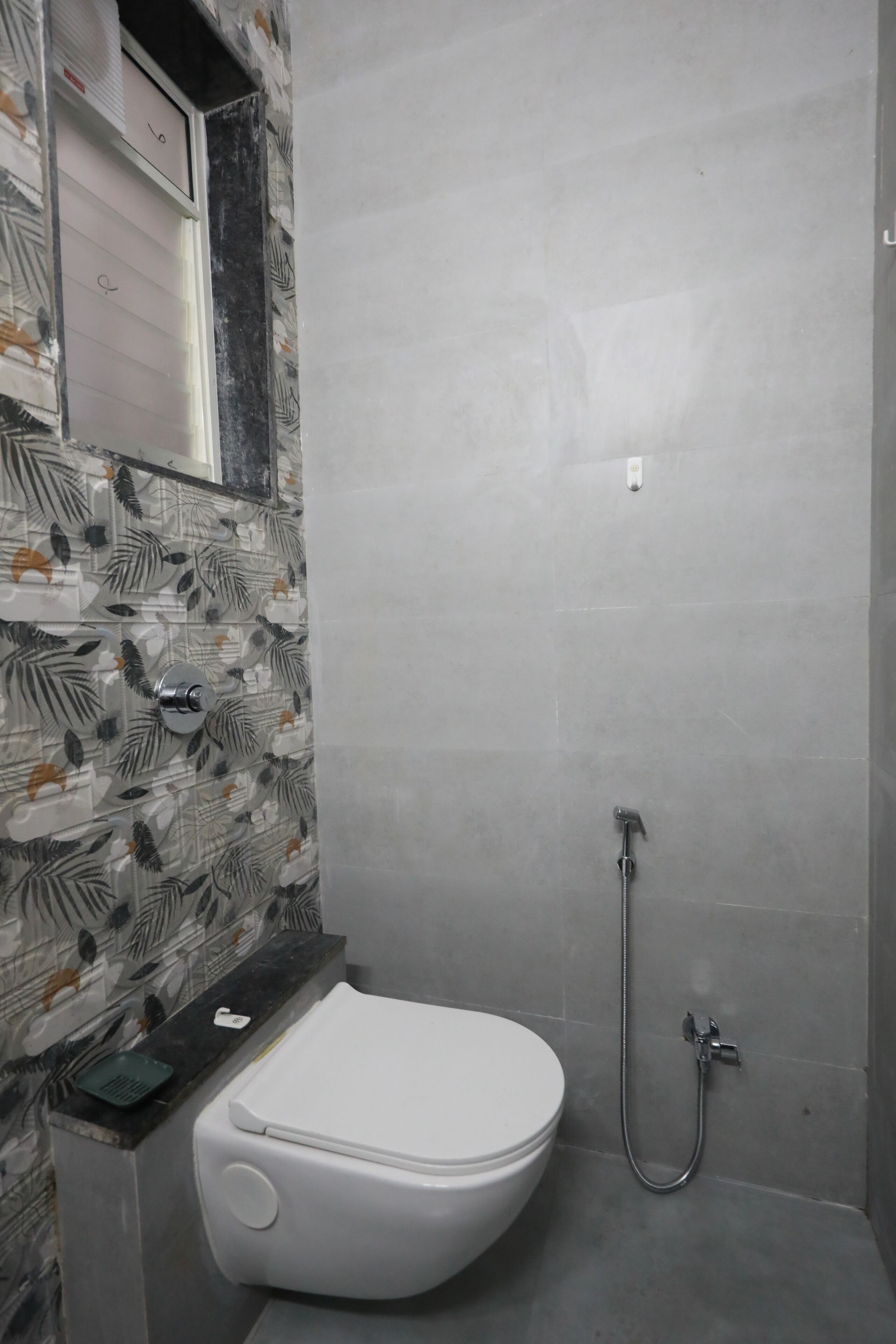 A bathroom with a toilet, a shower, and a tiled wall with a leaf pattern.