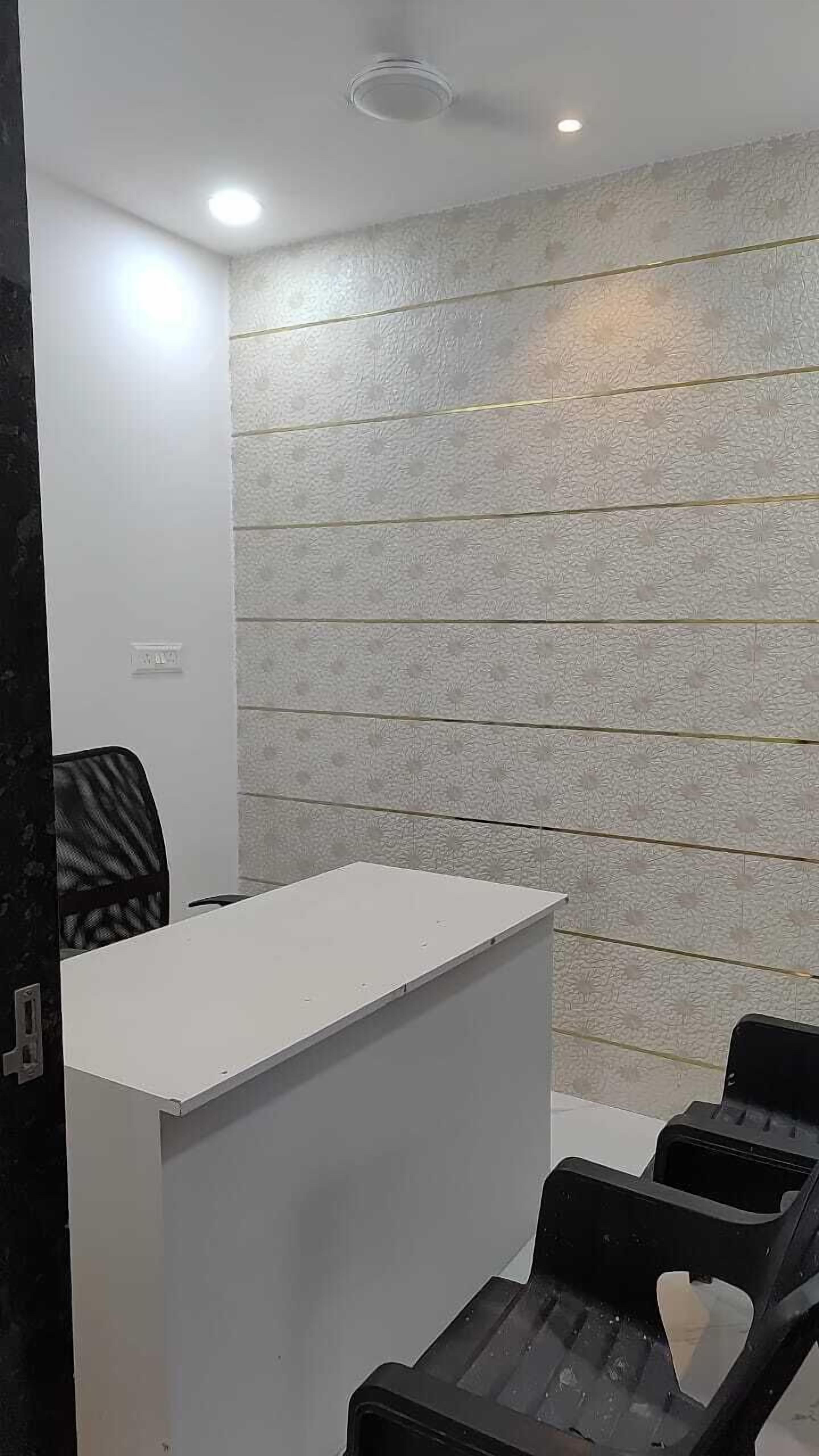 Un área de recepción con un escritorio blanco, sillas negras y un papel tapiz estampado.
