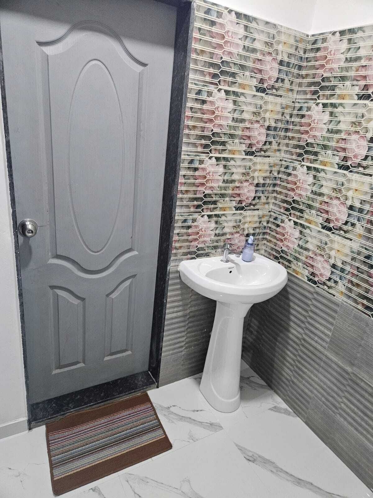 A bathroom with a gray door, a white sink, and a tiled wall with a floral pattern.