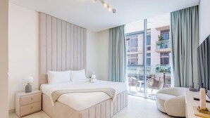 A modern bedroom with a large bed, a nightstand, a desk, and a view of the city through large windows.