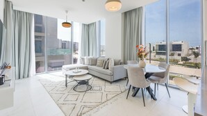 A modern living room with a sofa, dining table, and chairs, large windows with curtains, and a city view.