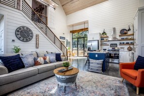 Uma sala de estar ampla com escada, cozinha equipada com eletrodomésticos modernos e um relógio grande na parede.