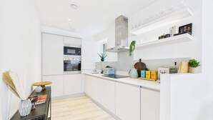 A modern kitchen with white cabinetry, a built-in oven, a coffee machine, and a shelf with glassware.