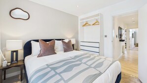 A modern bedroom with a large bed, bedside tables, a wardrobe, and a hallway leading to a bathroom.