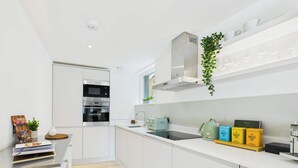 A modern kitchen with white cabinetry, a built-in oven, a stainless steel range hood, and a window above the sink. - Chic and cosy apartment near Borough Market (Greater London)