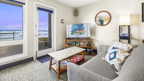 A living room with a view of the ocean, a television, a bookshelf, and a round mirror. - Ground Floor Studio, Oceanfront Patio, Kitchenette (Lincoln City)