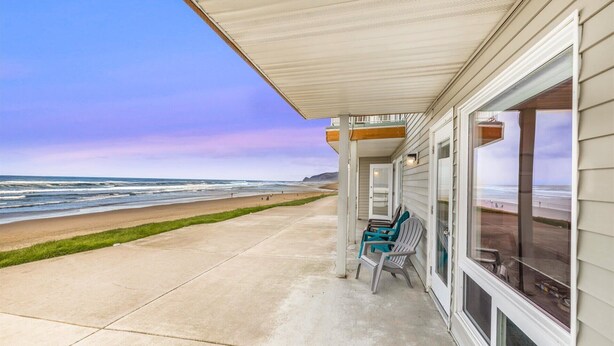 A beachfront property with a covered patio, a concrete walkway, and a view of the ocean. - Ground Floor Studio, Oceanfront Patio, Kitchenette (Lincoln City)
