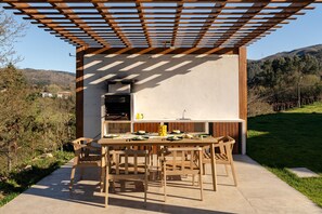 Eine Außenküche mit Tisch und Stühlen, ein überdachter Pergola-Bereich und Blick auf die umliegende Landschaft.