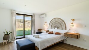 Un dormitorio con cama, mesitas de noche, un ventilador grande, una planta en maceta y vistas al exterior.