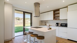 Una cocina moderna con una isla central, taburetes de bar y vistas a un paisaje verde.