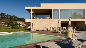 Una casa moderna con piscina, mobiliario de exterior y un muro de piedra.