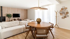Una sala de estar moderna con una mesa de comedor redonda de madera, un sofá blanco y un televisor de pantalla plana montado en la pared.