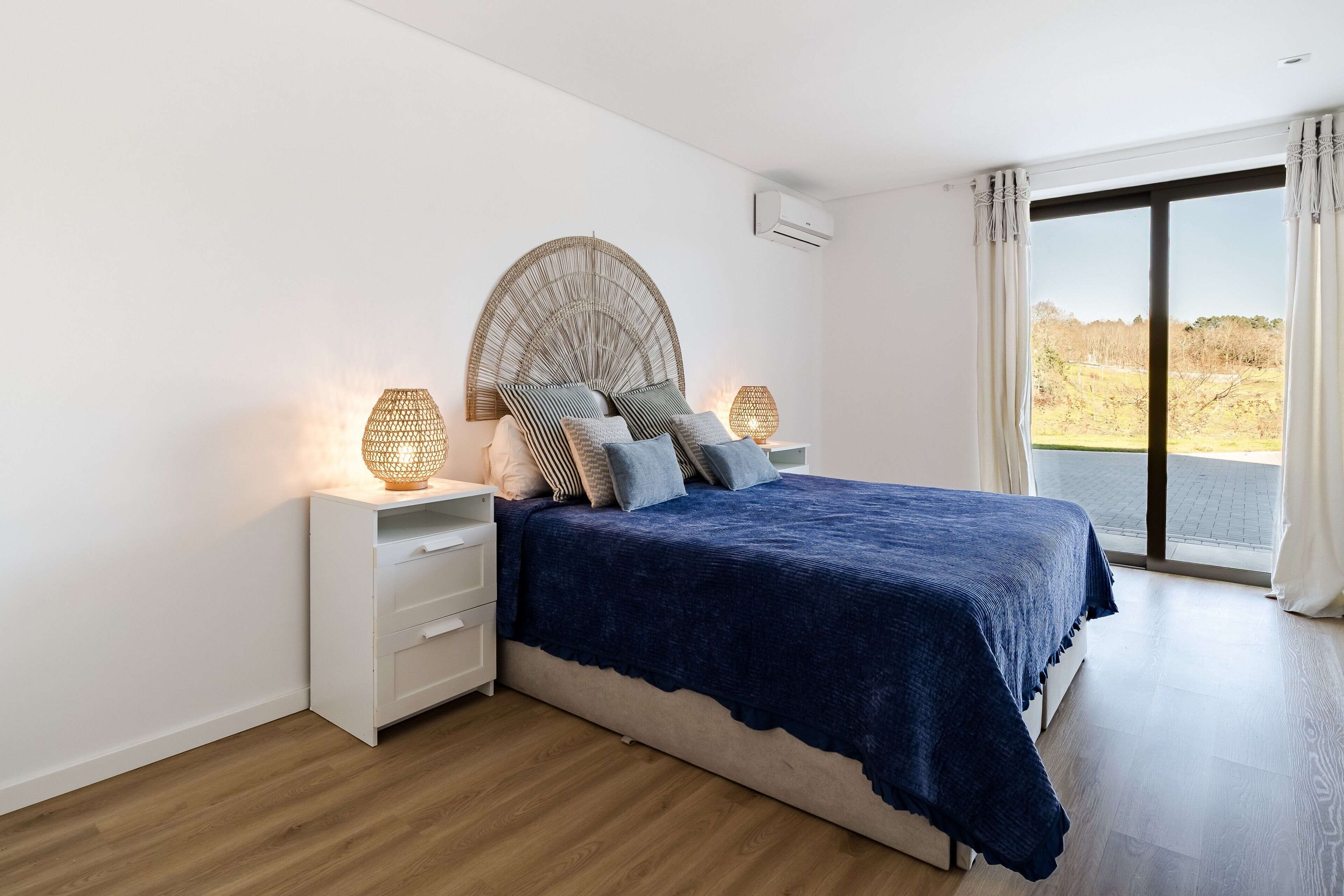 A bedroom with a bed, bedside lamps, a large window, and a view of the outdoors.