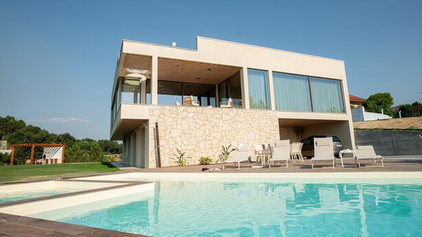 A modern two-story house with a swimming pool, outdoor seating, and a stone facade.
