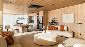 Ein modernes Wohnzimmer mit Sofa, Hocker, Essbereich, Küche und einem großen abstrakten Gemälde an der Wand.