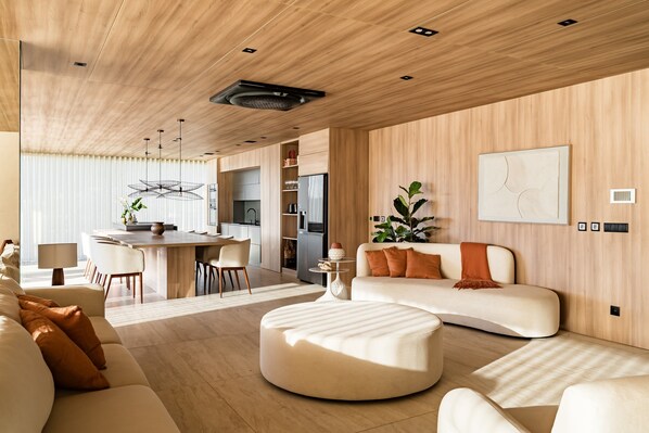 Una sala de estar moderna con sofá, reposapiés, comedor, cocina y un cuadro abstracto grande en la pared.