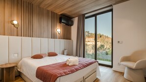 Ein modernes Hotelzimmer mit einem großen Bett, einer Sitzecke und Blick auf eine gebirgige Landschaft.