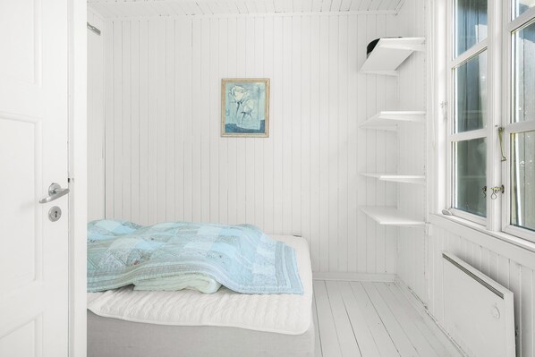 A white room with a bed, a framed picture on the wall, and a window with blinds. - Unique and private summer house (Skagen)