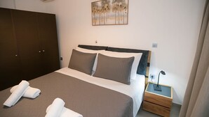 Un lit bien fait, avec deux oreillers, une table de chevet sur laquelle se trouve une lampe, et un tableau accroché au mur.