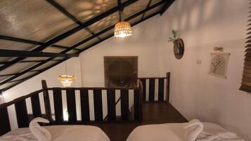 Una habitación con dos camas, un banco de madera, una lámpara colgante y una ventana con persianas.