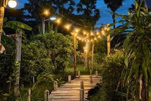 A wooden pathway leading through a lush garden at night, illuminated by string lights. - AUN-I-NA Home stay at Nakhon Phanom (Nakhon Phanom)