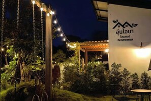 Un espace extérieur aménagé avec des guirlandes lumineuses, une pergola et un panneau avec des caractères thaïlandais.