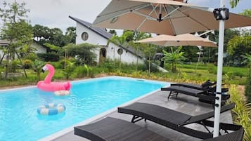 A swimming pool with lounge chairs and umbrellas, surrounded by greenery.