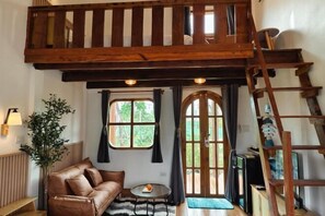 Ein gemütliches Zimmer mit einem Schlafzimmerboden aus Holz, einem braunen Ledersofa, einem kleinen runden Tisch und einem großen, bogenförmigen Fenster.