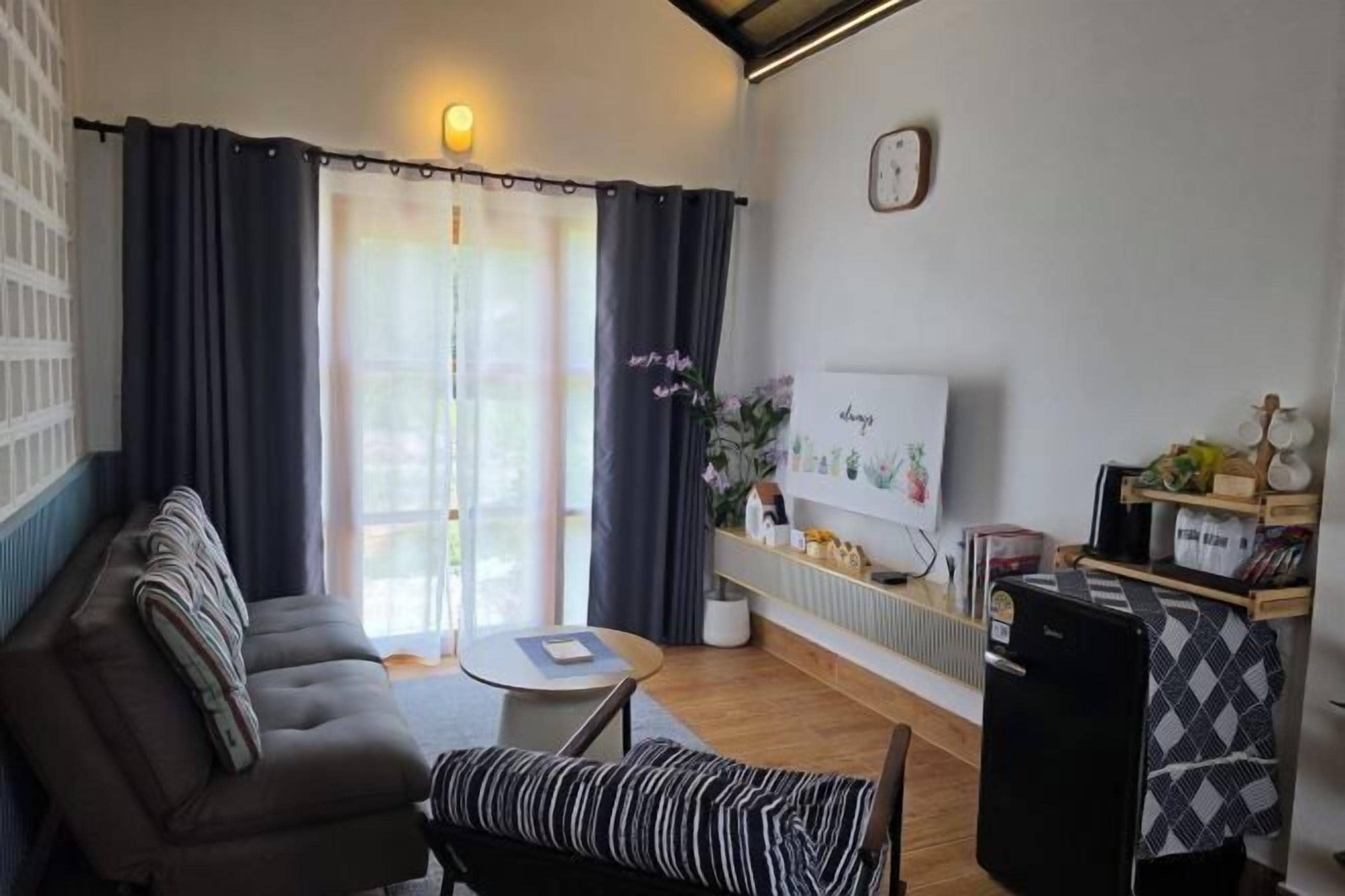 A living room with a sofa, a bench, a small table, a TV, and a refrigerator.