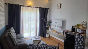 A living room with a sofa, a bench, a small table, a TV, and a refrigerator.