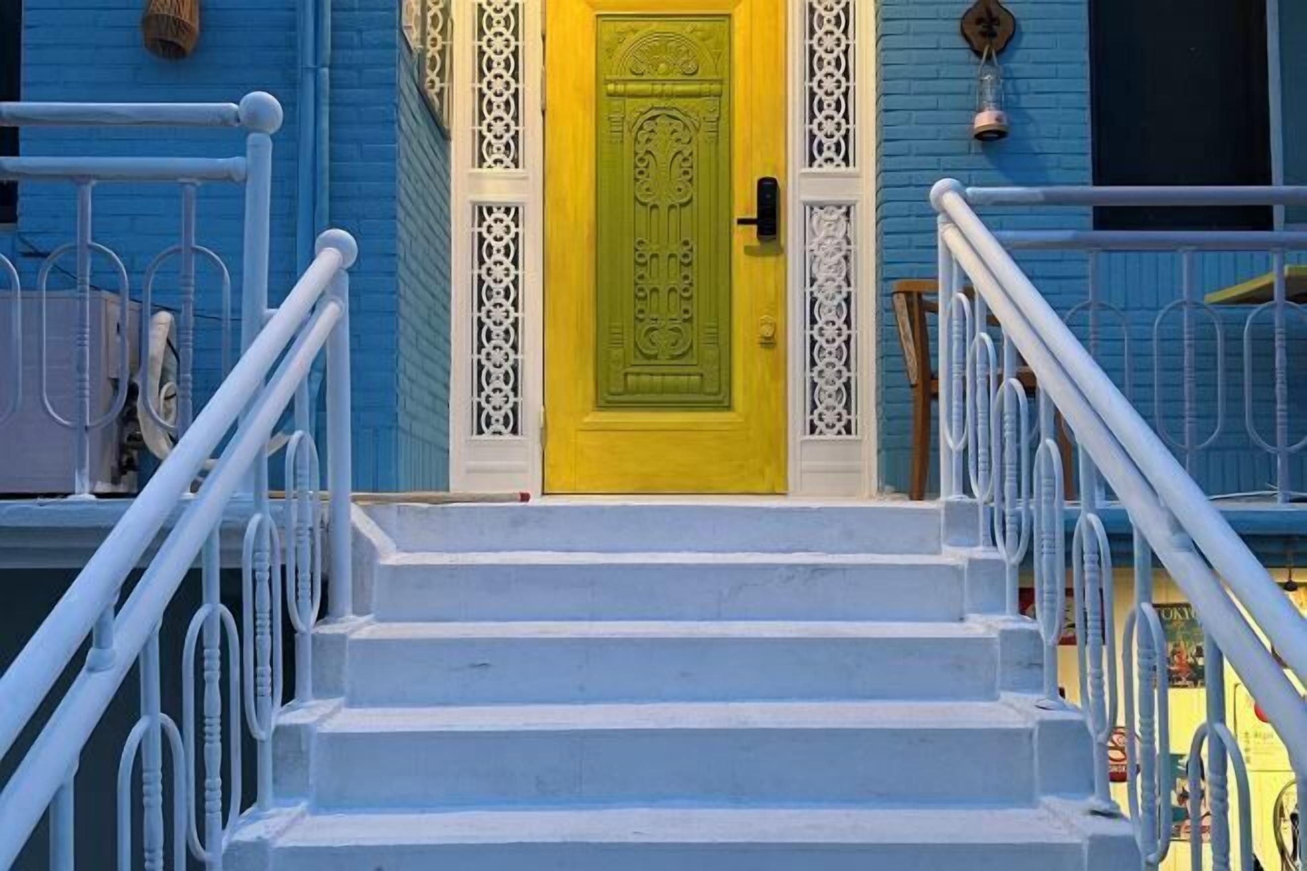 A set of white stairs leading to a yellow door with intricate designs, flanked by white railings.