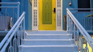 A set of white stairs leading to a yellow door with intricate designs, flanked by white railings.